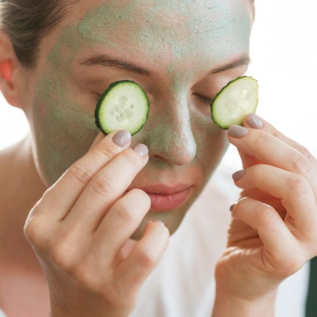 woman with facial mask putting slices cucumber