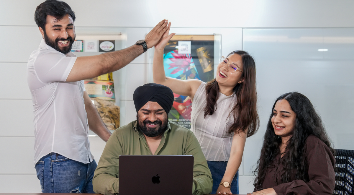 Group of diverse people smiling and high-fiving around a laptop in a modern office