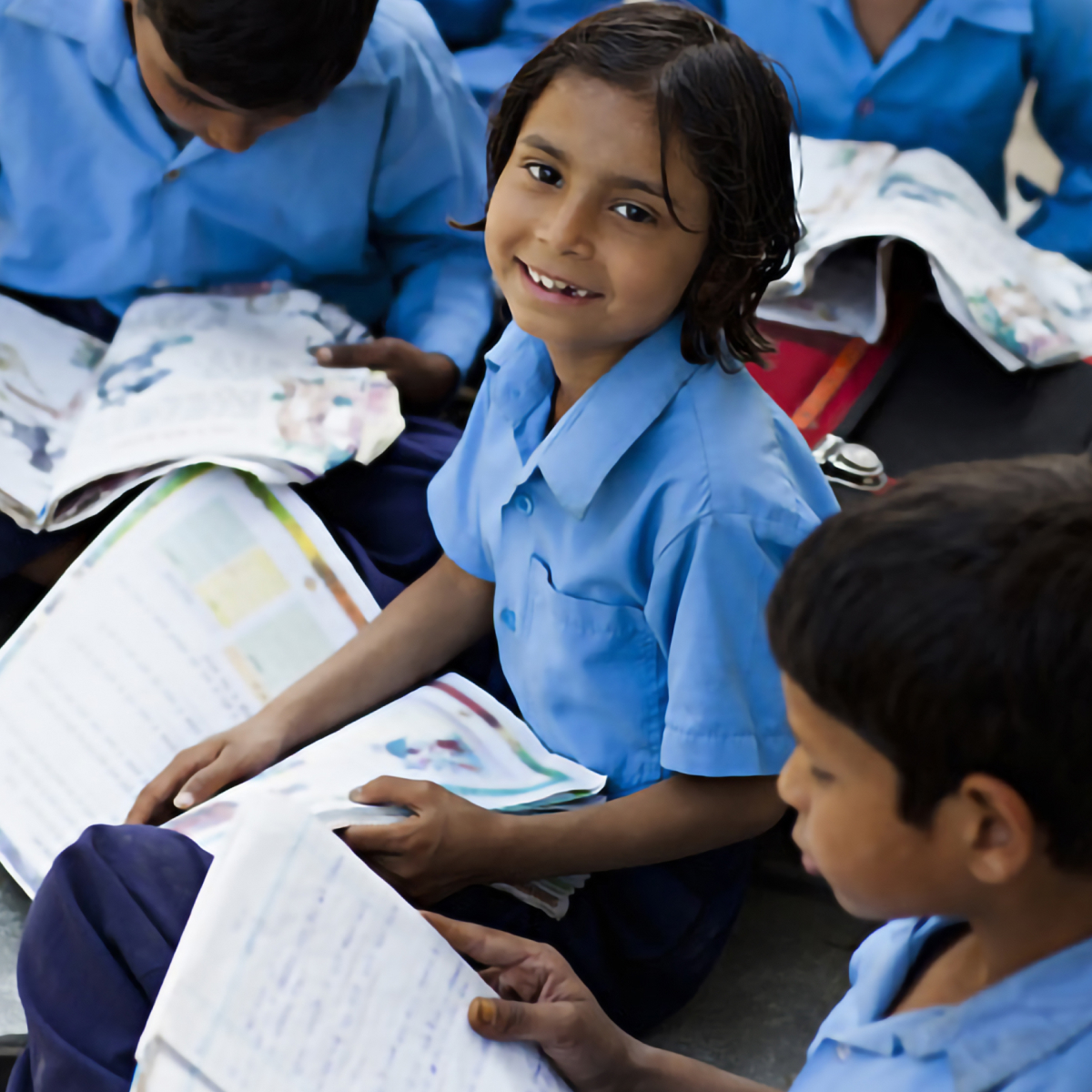 Children in blue school uniforms studying and smiling while sitting on the floor